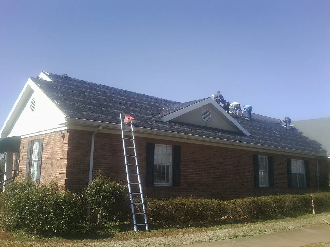 Crew tearing shingles off a brick ranch roof with a ladder set — Metal Roof Repair work by our crew in Garfield