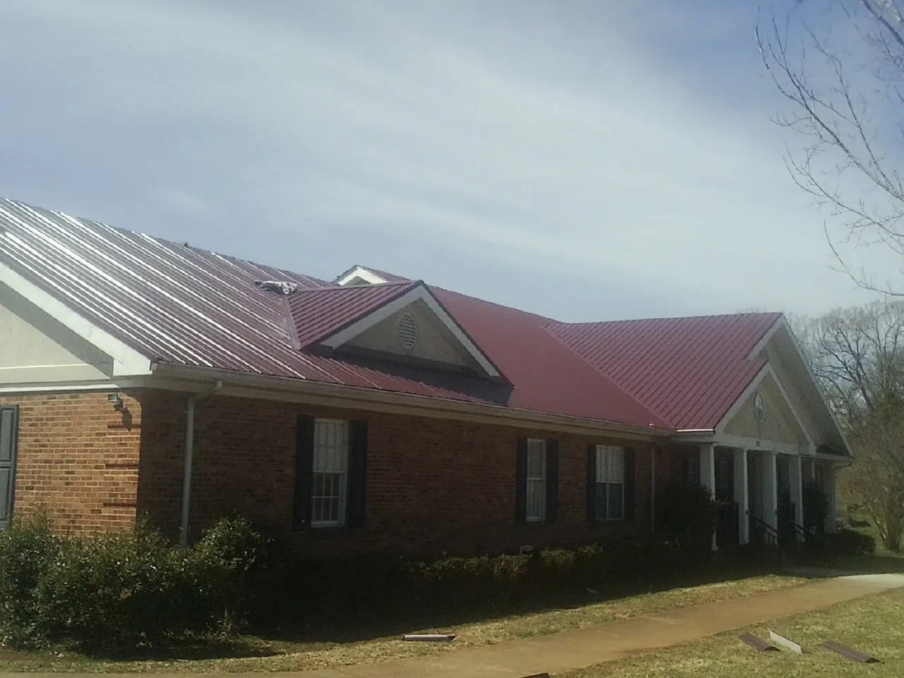 Red metal roof with gabled entries on a long brick building, from a Hail Damage Roof Repair job in Garfield